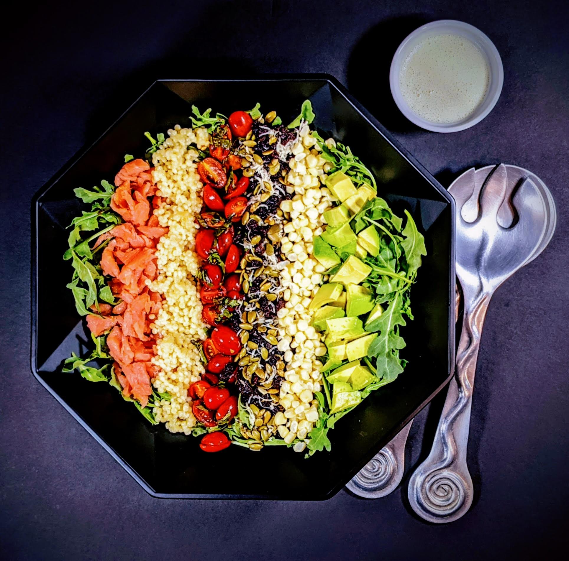 salmon chopped salad in black bowl and silver salad tossers